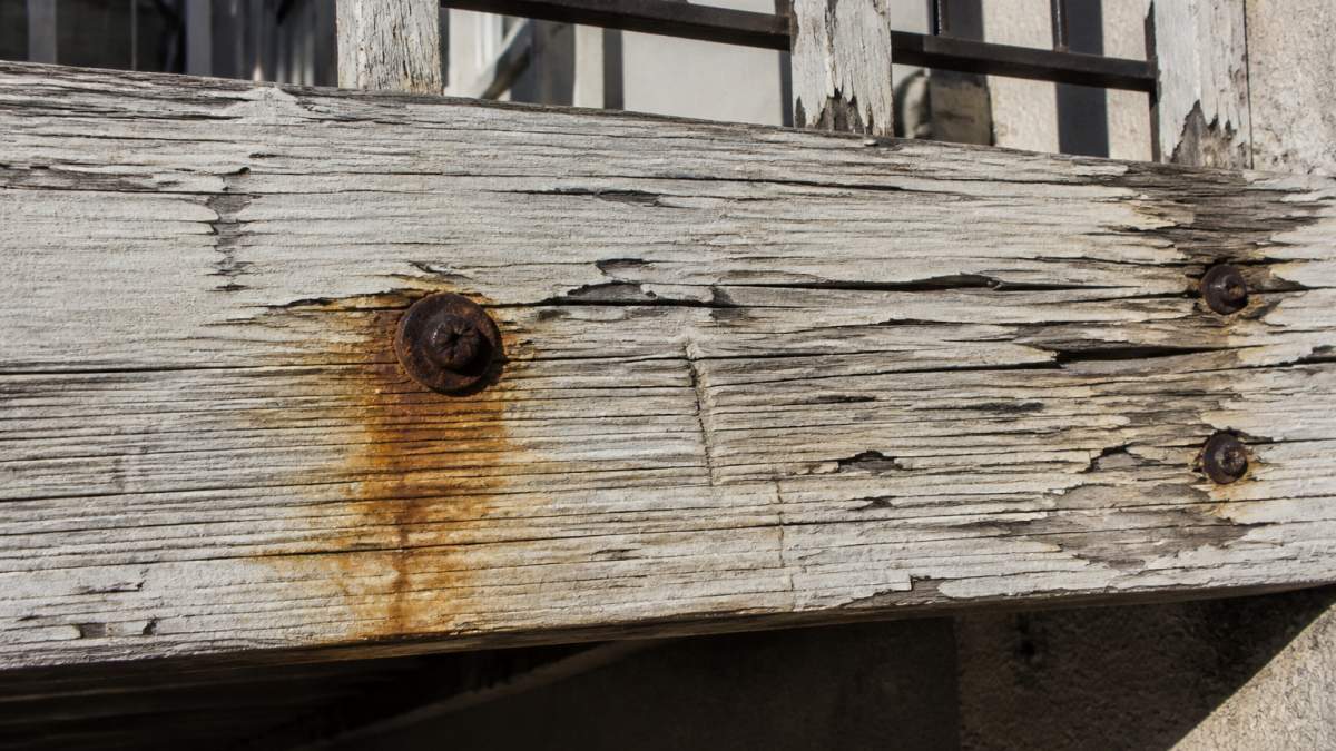 Weathered wooden ledger board with rust stains around lag bolts, indicating risk of a potential balcony collapse.